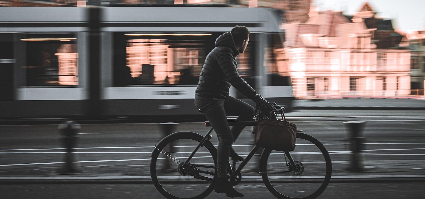 Mann geschäftlich auf Fahrrad, im Hintergrund fahrende Straßenbahn