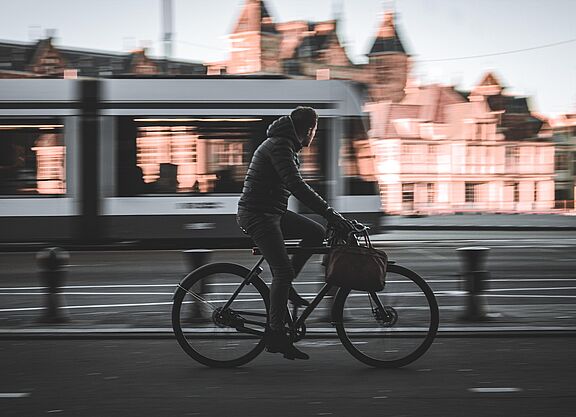 Mann geschäftlich auf Fahrrad, im Hintergrund fahrende Straßenbahn